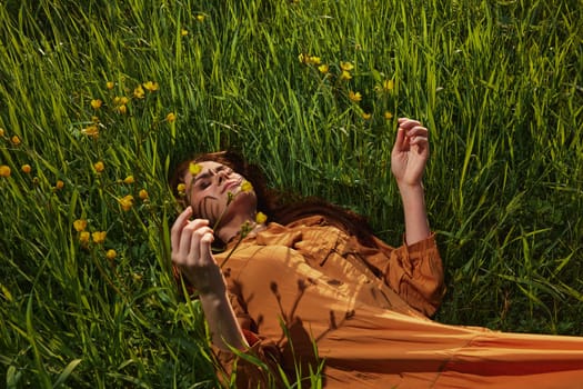 a calm woman with long red hair lies in a green field with yellow flowers, in an orange dress with her eyes closed, with a pleasant smile on her face, enjoying peace and recuperating, illuminated by the setting sun. High quality photo