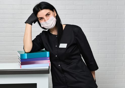 Medical staff, student medic intern, beautiful female doctor dentist in black uniform, with a stack of books and medical encyclopedias. Knowledge, education, library, health care and welfare concept