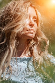 Portrait of a blonde in the park. Happy woman with long blond hair in a blue dress