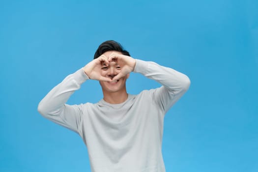 A handsome man showing arms heart cover eye isolated over blue color background