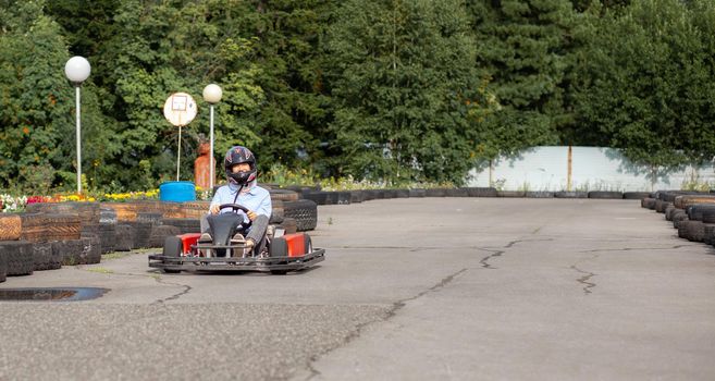 A girl or a woman in a hard hat rides a go-kart on a special track fenced with rubber wheels. Active recreation and sports on transport. Preparation and training for competitions. 