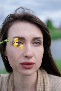 portrait of beautiful brunette woman with yellow small wildflower. skin care, nature.