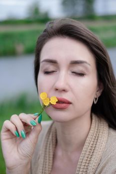 portrait of beautiful brunette woman with yellow small wildflower. skin care, nature.