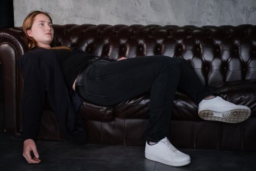 beautiful confident brunette woman in black on a brown leather couch in grey dark room. business woman. feminine. millennial people.