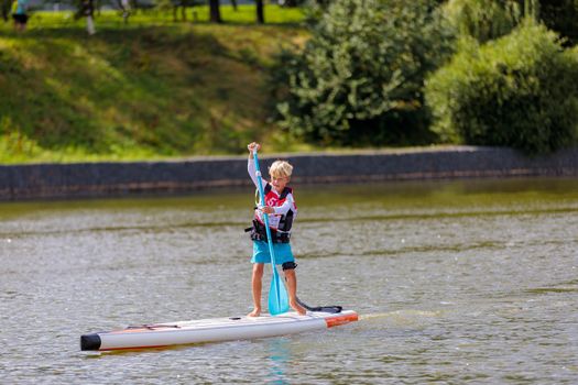 A child swims on a surfboard, pushing off with a paddle. Paddleboarding. Russia Zelenograd 14 August 2021