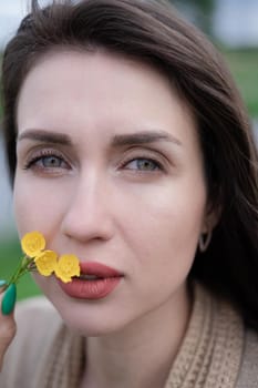 portrait of beautiful brunette woman with yellow small wildflower. skin care, nature.