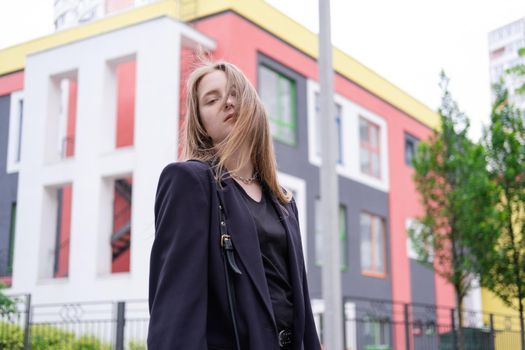 portrait of confident attractive brunette woman in black on background of colorful bright buildings. business woman. feminine. millennial people.