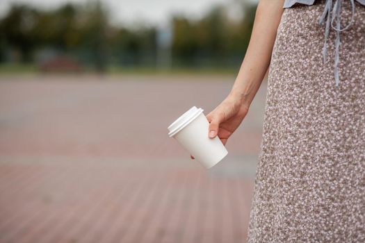 White paper cup with coffee in woman hand. Time for drink coffee in city. Coffee to go. Enjoy moment, take a break. Disposable paper cup closeup. Delicious hot beverage. Blank space for text, mockup