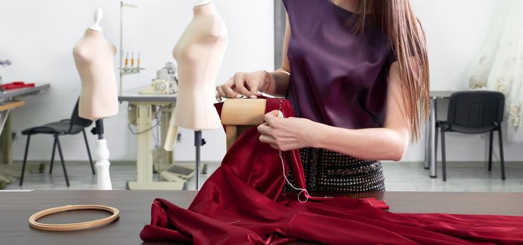 Beautiful young dressmaker in workroom sewing red dress