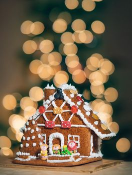 Christmas gingerbread house decoration on background of defocused golden lights of Christmas tree. Vertical. Copy space. Gingerbread house cake with bokeh as concept Christmas, Happy new year holidays