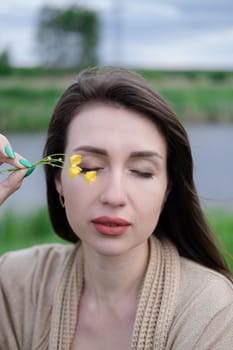 portrait of beautiful brunette woman with yellow small wildflower. skin care, nature.