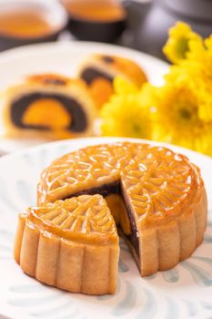 Mid-Autumn Festival traditional food concept - Beautiful cut moon cake on blue pattern plate on white background with flower, close up, copy space