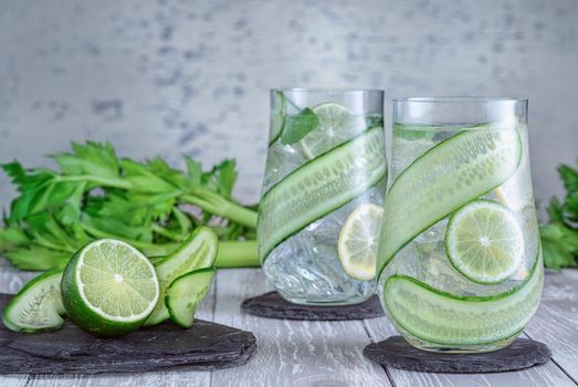 Glass with fresh organic detox cucumber water with lime and lemon on grey background.