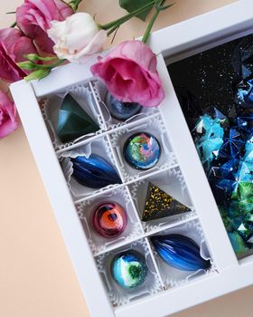 Gift box of handmade chocolates. Geometric and space design. Box on a light background. Sweets and candies close-up. Vertical photo