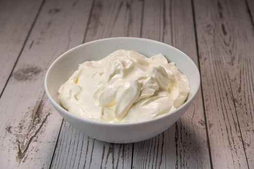 Whipped cream in a white bowl, Dairy product, healthy eating theme, wooden table background. High quality photo