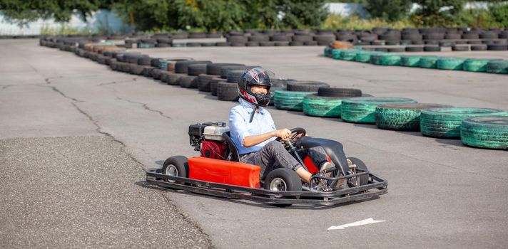 A girl or a woman in a hard hat rides a go-kart on a special track fenced with rubber wheels. Active recreation and sports on transport. Preparation and training for competitions. 