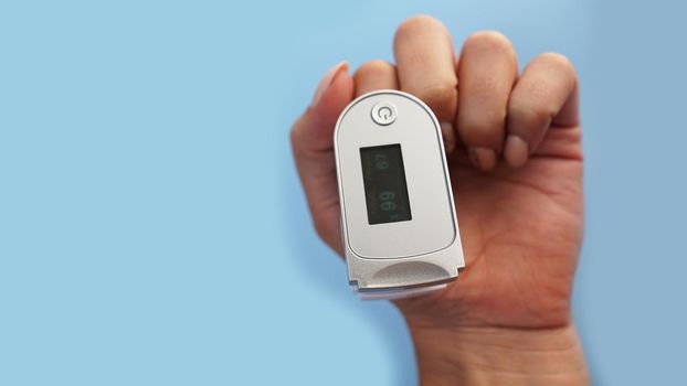 Medical device for hypoxia. Female finger in a pulse oximeter on a blue background with copyspace