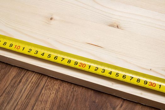 Measuring a wooden board with an yellow tape measure close up
