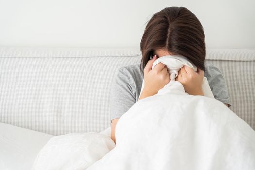 upset young brunette woman sitting on the white linen in bed at home, copyspace for your text to the left