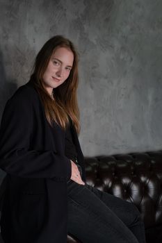 portrait of beautiful confident brunette woman in black in grey dark room. business woman. feminine. millennial people. stylish fashion clothes.