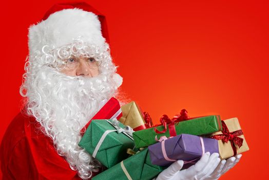 Happy Santa Claus with gift boxes in hands on red background with copy space. Christmas gifts concept