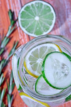 Glass with fresh organic detox cucumber water with lime and lemon on wooden background.
