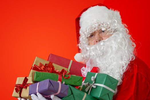 Happy Santa Claus with gift boxes in hands on red background with copy space. Christmas gifts concept