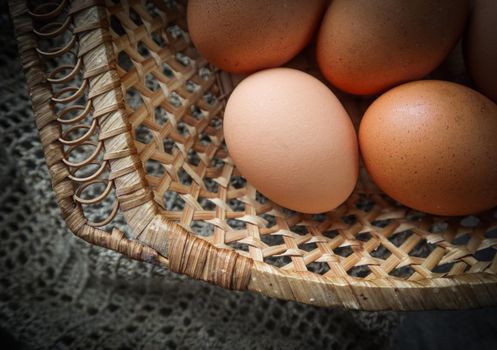 Top view of eggs in a straw basket on a natural linen napkins and a rustic wooden background