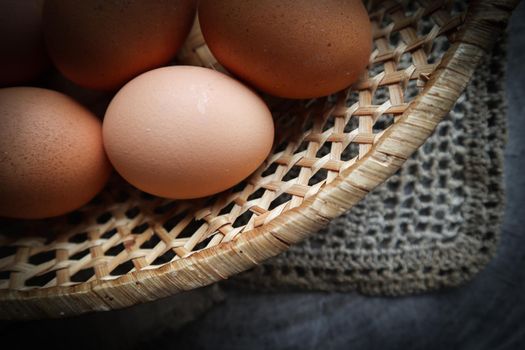 Top view of eggs in a straw basket on a natural linen napkins and a rustic wooden background