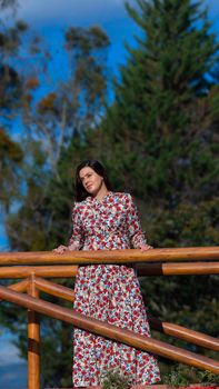 Portrait of beautiful young Latin woman looking to the left with floral design dress standing in the middle of a garden with a background of trees during the morning