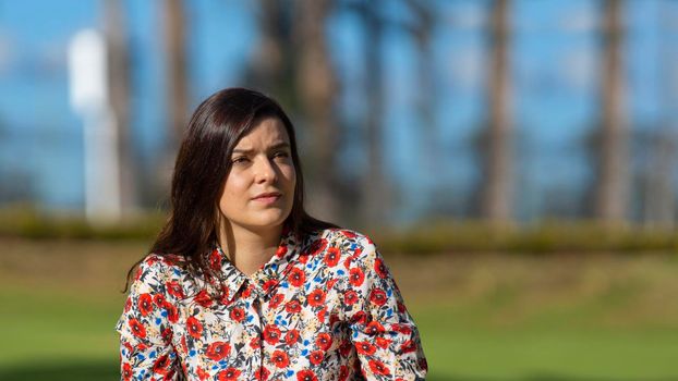 Portrait of beautiful young Latin woman looking to the right with floral design dress sitting in the middle of a garden with a background of trees during the morning