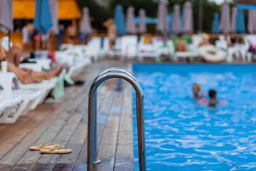 Ladder stainless handrails for descent into swimming pool. Swimming pool with handrail . Ladder of a swimming pool. People swim and relax in the pool