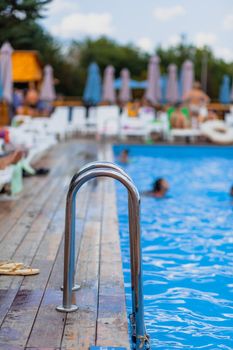 Ladder stainless handrails for descent into swimming pool. Swimming pool with handrail . Ladder of a swimming pool. People swim and relax in the pool