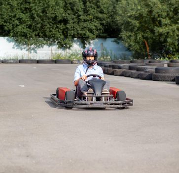 A girl or a woman in a hard hat rides a go-kart on a special track fenced with rubber wheels. Active recreation and sports on transport. Preparation and training for competitions. 