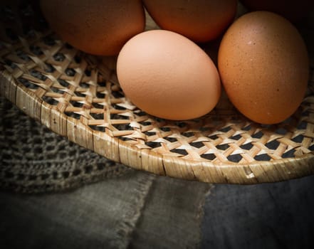 Top view of eggs in a straw basket on a natural linen napkins and a rustic wooden background