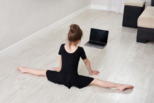 Little girl doing gymnastics exercises at home using online learning 