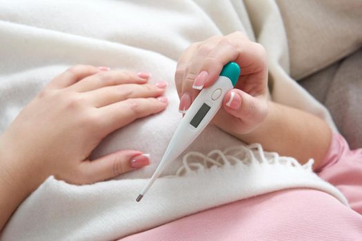 Woman looking at thermometer. Female hands holding a digital thermometer. Girl measures the temperature. Concept of fever, flue or virus