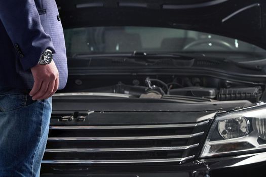 Man looking on the engine of a car with open hood in auto repair shop