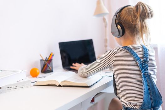Little girl doing her homework at home and using a laptop