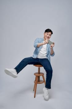 Portrait of an excited young man sitting on a stool and playing games on mobile phone