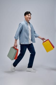 happy young man holding colorful paper bags while looking at camera 
