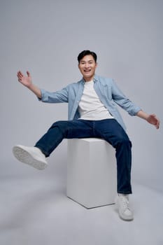 Smiling Happy Asian man sitting on the cube in studio with white background