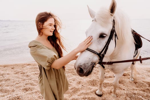 A woman in a dress stands next to a white horse on a beach, with the blue sky and sea in the background