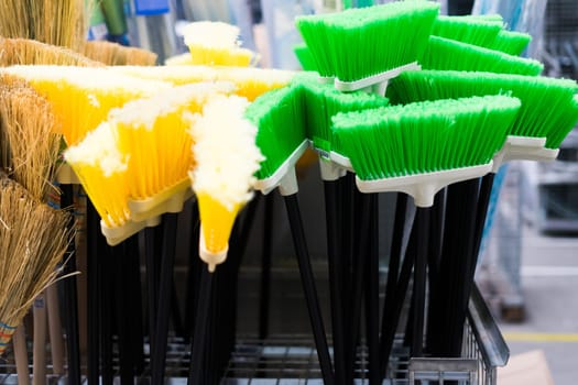 Plastic brushes for cleaning premises. Assortment of multi-colored brooms in store. Close-up