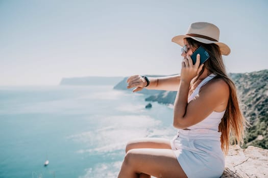 Successful business woman in yellow hat working on laptop by the sea. Pretty lady typing on computer at summer day outdoors. Freelance, travel and holidays concept.