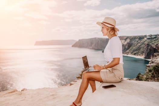 Digital nomad, Business woman working on laptop by the sea. Pretty lady typing on computer by the sea at sunset, makes a business transaction online from a distance. Freelance remote work on vacation