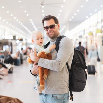 Father traveling with child, holding his infant baby boy at airport terminal waiting to board a plane. Travel with kids concept