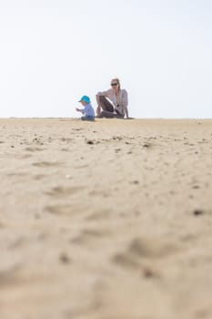 Mother playing his infant baby boy son on sandy beach enjoying summer vacationson on Lanzarote island, Spain. Family travel and vacations concept. Copy space.