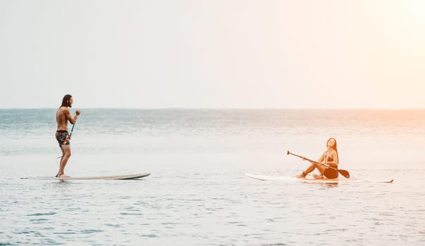 Sea woman and man on sup. Silhouette of happy young woman and man, surfing on SUP board, confident paddling through water surface. Idyllic sunset. Active lifestyle at sea or river