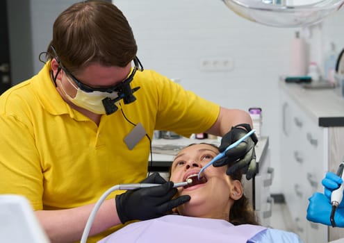 Experienced professional dentist wearing orthodontist binoculars, examines teeth, performs treatment to a patient using dental mirror, probe and drill. The concept of dental checkup in pregnancy time